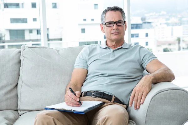 Man op de bank zitten en schrijven over Kladblok — Stockfoto