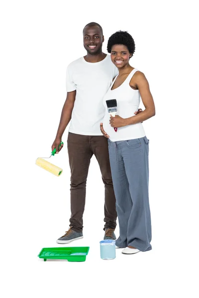 Pregnant couple holding roller paint and paint brush — Stock Photo, Image