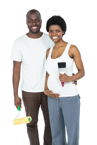 Pregnant couple holding roller paint and paint brush — Stock Photo, Image