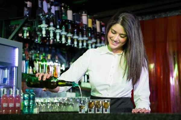 Pretty bartender pouring tequila into glasses — Stock Photo, Image