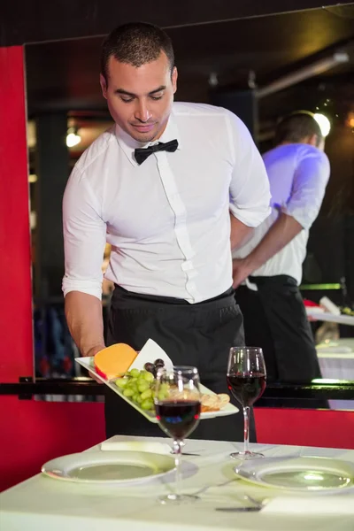 Официант, подающий фрукты и красное вино на столе — стоковое фото