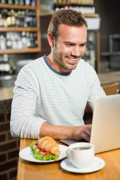 Man using laptop and having a croissant — Stock Photo, Image