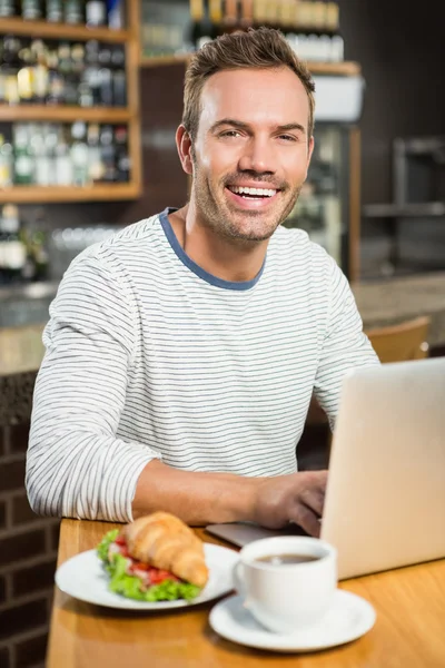 Uomo utilizzando il computer portatile e avere un croissant — Foto Stock