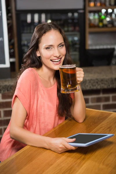 Красивая женщина пьет пиво и смотрит на планшет — стоковое фото