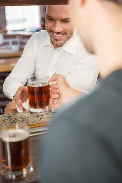 Handsome bar tender giving a pint to customer — Stock Photo, Image