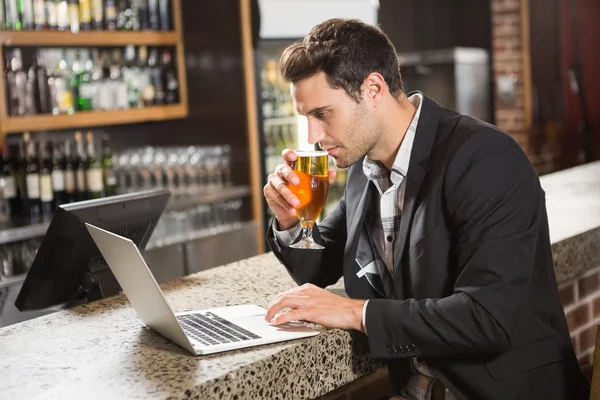 Beau mec utilisant un ordinateur portable et prenant une bière — Photo