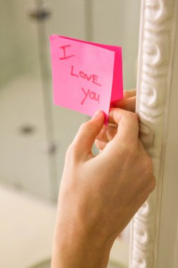 Woman sticking I love you note on mirror clipart