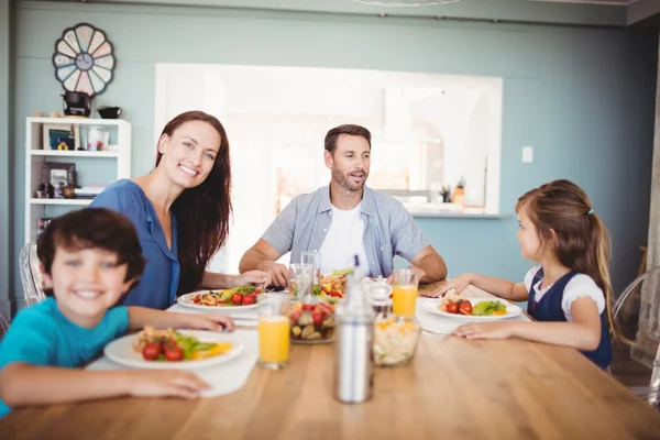 Família sorridente com comida na mesa de jantar — Fotografia de Stock