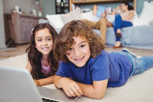 Siblings lying by laptop on carpet — Stock Photo, Image