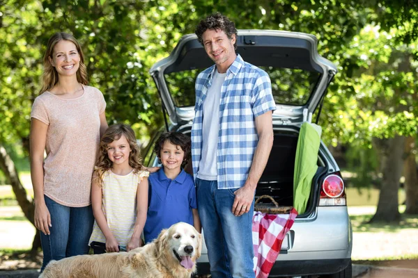 Sorrindo família de pé na frente de um carro — Fotografia de Stock