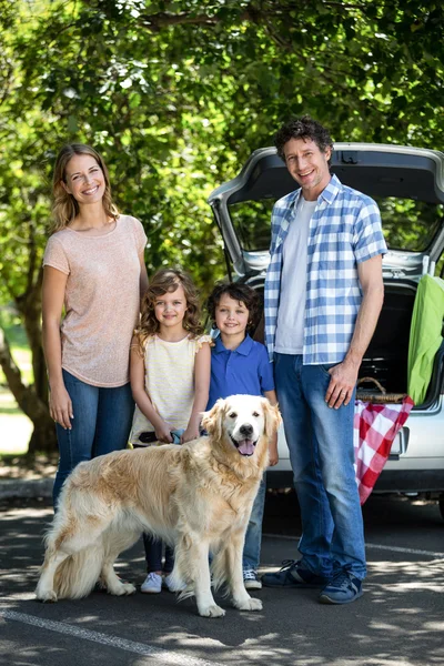 Familia sonriente de pie frente a un coche — Foto de Stock