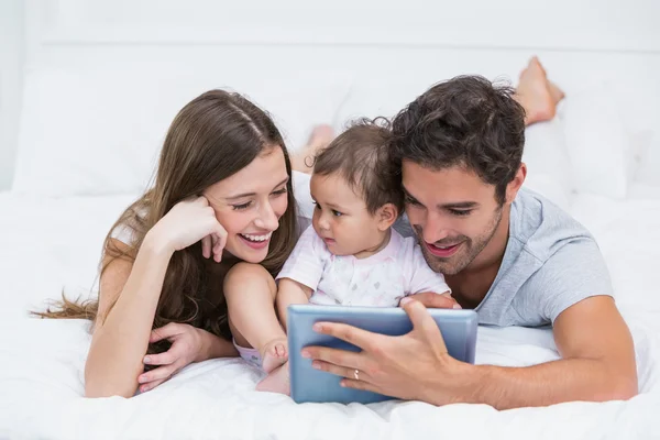 Молодая семья смотрит на цифровую табличку на кровати — стоковое фото