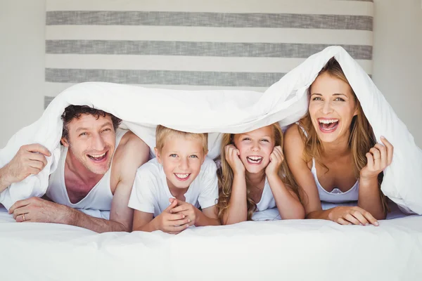 Familia cubierta con edredón en la cama — Foto de Stock