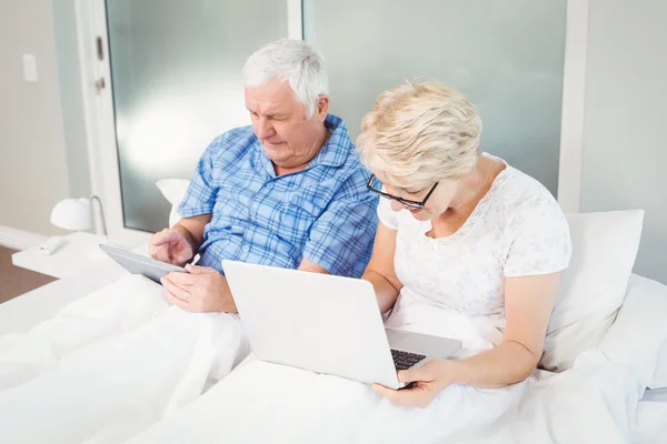 Äldre par med teknik på sängen — Stockfoto