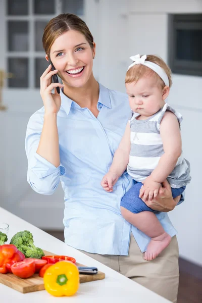 Woman with cellphone carrying daughter — Stock Photo, Image