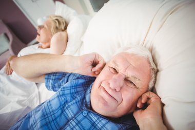 man covering ears from snoring wife clipart