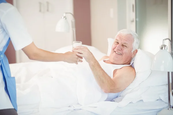 Enfermera dando vaso de agua a hombre mayor — Foto de Stock