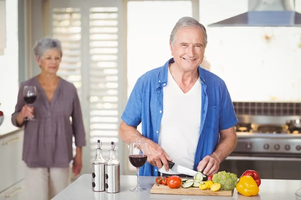 Man cutting vegetables with wife in backgroun — Stock Photo, Image