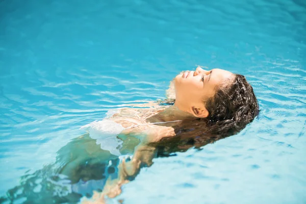 Mujer flotando en la piscina con los ojos cerrados —  Fotos de Stock