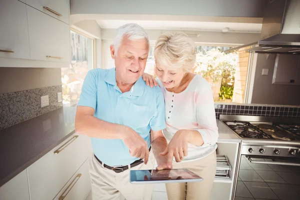 Feliz pareja de ancianos sosteniendo tableta digital en la cocina — Foto de Stock