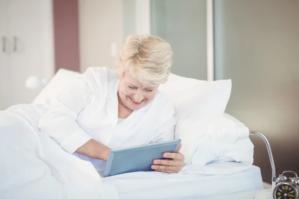 Seniorin nutzt digitales Tablet während sie im Bett liegt — Stockfoto