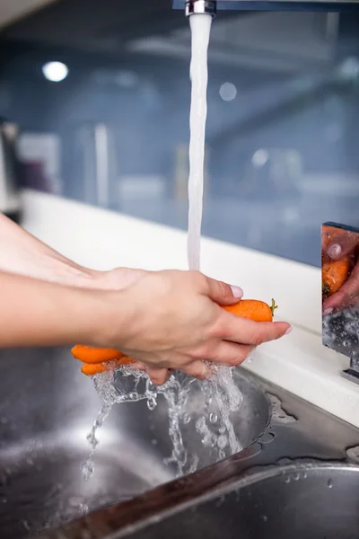 Woman cleaning carrots at washbasin — Stock Photo, Image