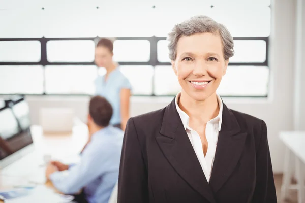 Zufriedene Geschäftsfrau mit Kollegen, die im Hintergrund arbeiten — Stockfoto