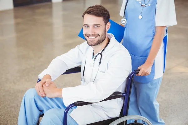 Doctor sitting on wheelchair with colleague — Stock Photo, Image