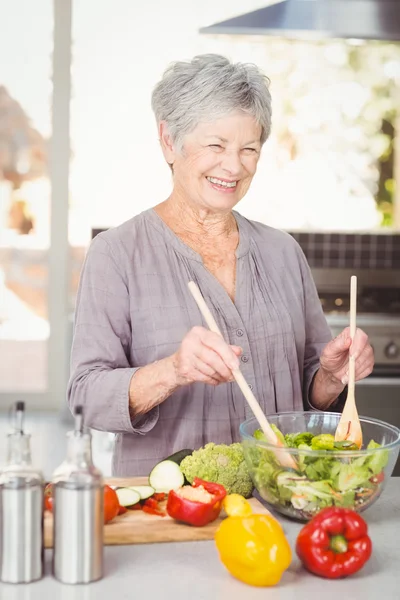 Donna gettando insalata mentre in piedi in cucina — Foto Stock