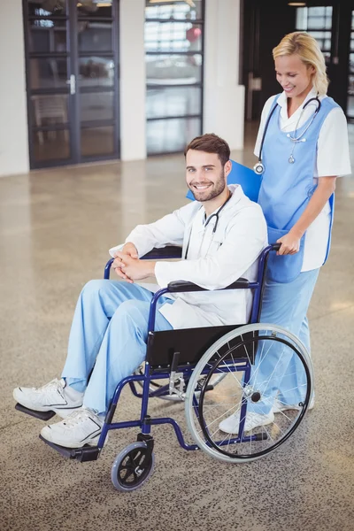 Doctor sitting on wheelchair with female colleague — Stock Photo, Image