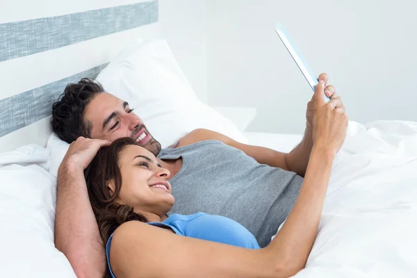 Casal usando tablet enquanto deitado na cama — Fotografia de Stock