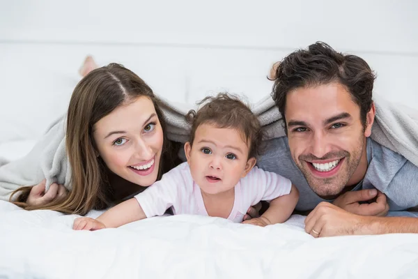 Portrait of happy couple with baby lying on bed — Stock Photo, Image