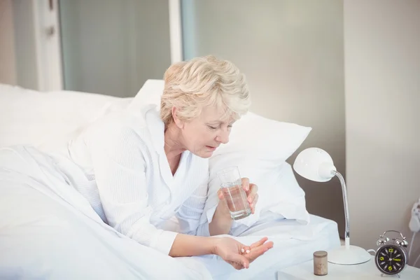 Woman taking medicine while resting on bed — Stock Photo, Image