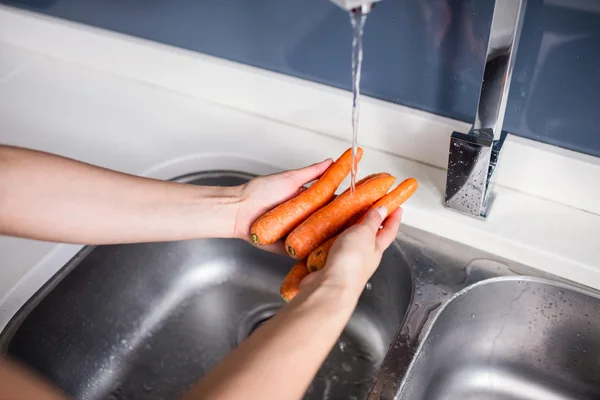 Woman washing carrots at kitchen sink — Stock Photo, Image
