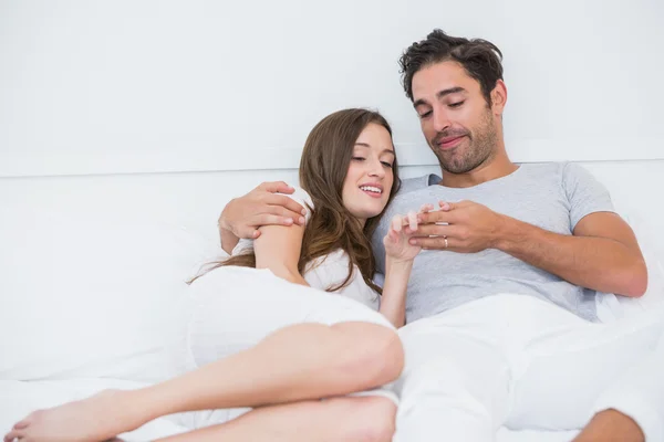 Couple looking at wedding ring while relaxing on bed — Stock Photo, Image