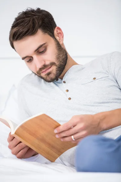 Muž, čtení knihy na posteli doma — Stock fotografie