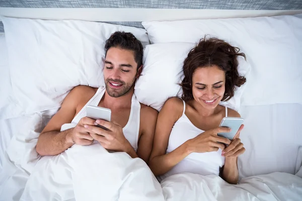 Casal usando smartphone na cama — Fotografia de Stock