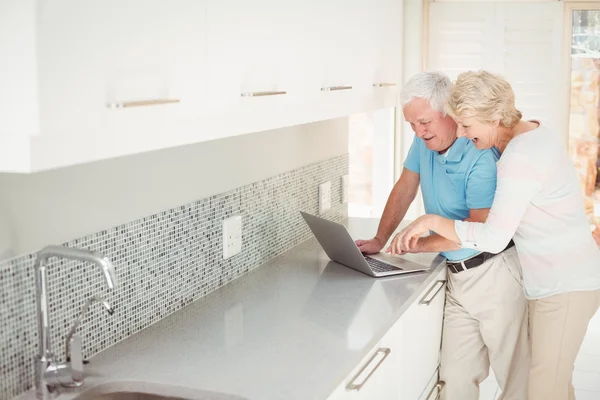 Feliz pareja de ancianos utilizando el ordenador portátil en la cocina — Foto de Stock