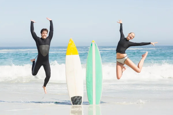 Casal animado pulando ao lado de pranchas de surf — Fotografia de Stock