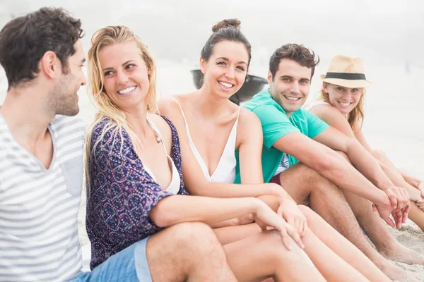 Groupe d'amis assis côte à côte sur la plage — Photo