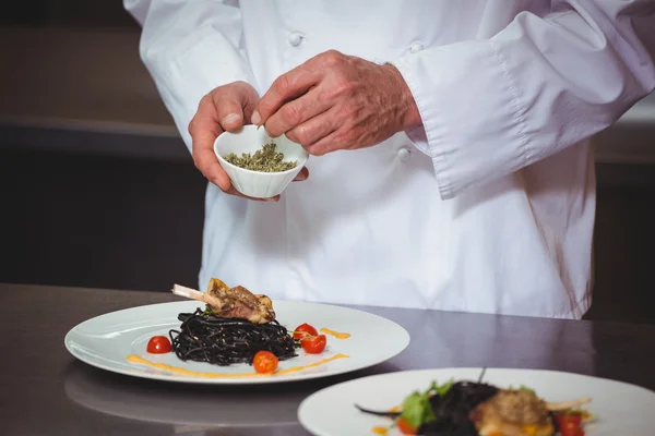 Chef sprinkling spices on dish — Stock Photo, Image