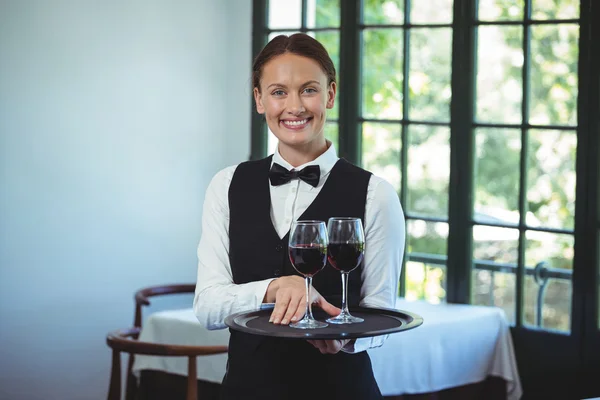 Uśmiechnięta kelnerka trzyma tacę z szklanki czerwonego wina — Zdjęcie stockowe
