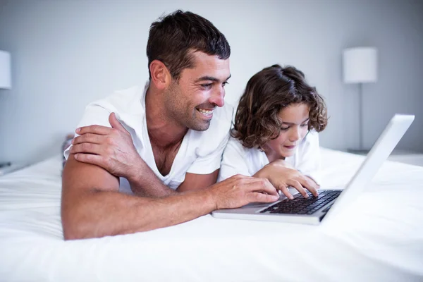 Отец и сын используют ноутбук на кровати — стоковое фото