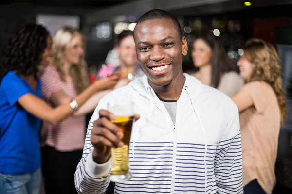 Smiling man showing a beer with his friends — Stock Photo, Image