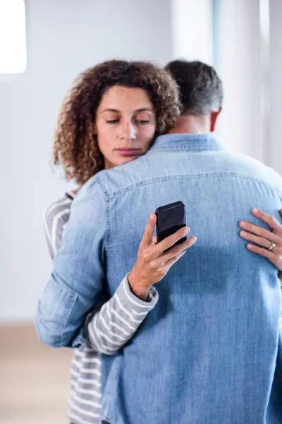 Mulher verificando seu telefone celular enquanto abraça um homem — Fotografia de Stock