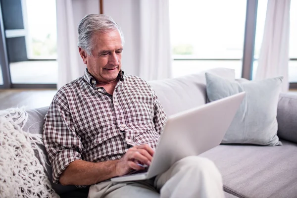 Пожилой мужчина с ноутбуком в гостиной — стоковое фото