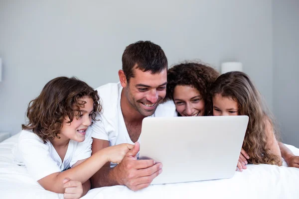 Счастливая семья с ноутбуком на кровати — стоковое фото