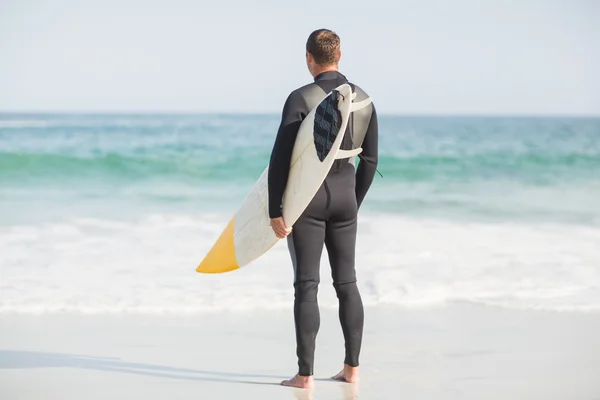 Серфер стоит на пляже с доской для серфинга — стоковое фото