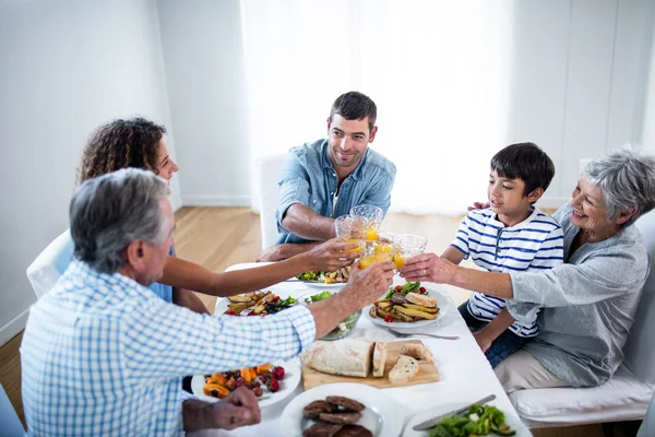 Family toasting glasses of orange juice while having breakfast — Stock Photo, Image