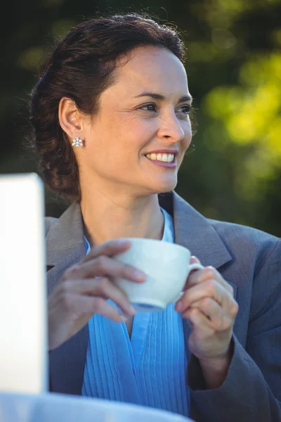 Mujer de negocios sonriente bebiendo café con portátil — Foto de Stock